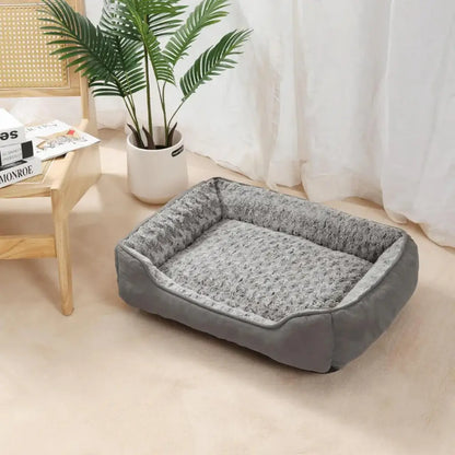 Gray pet bed on a beige floor with a plant and wooden furniture in the background