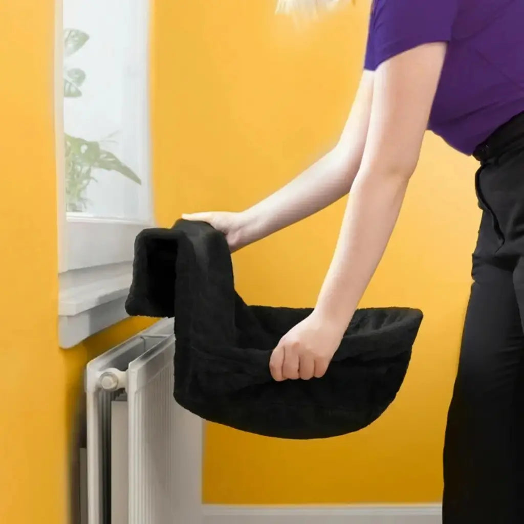 Person attaching a black pet bed against a yellow wall with a white radiator