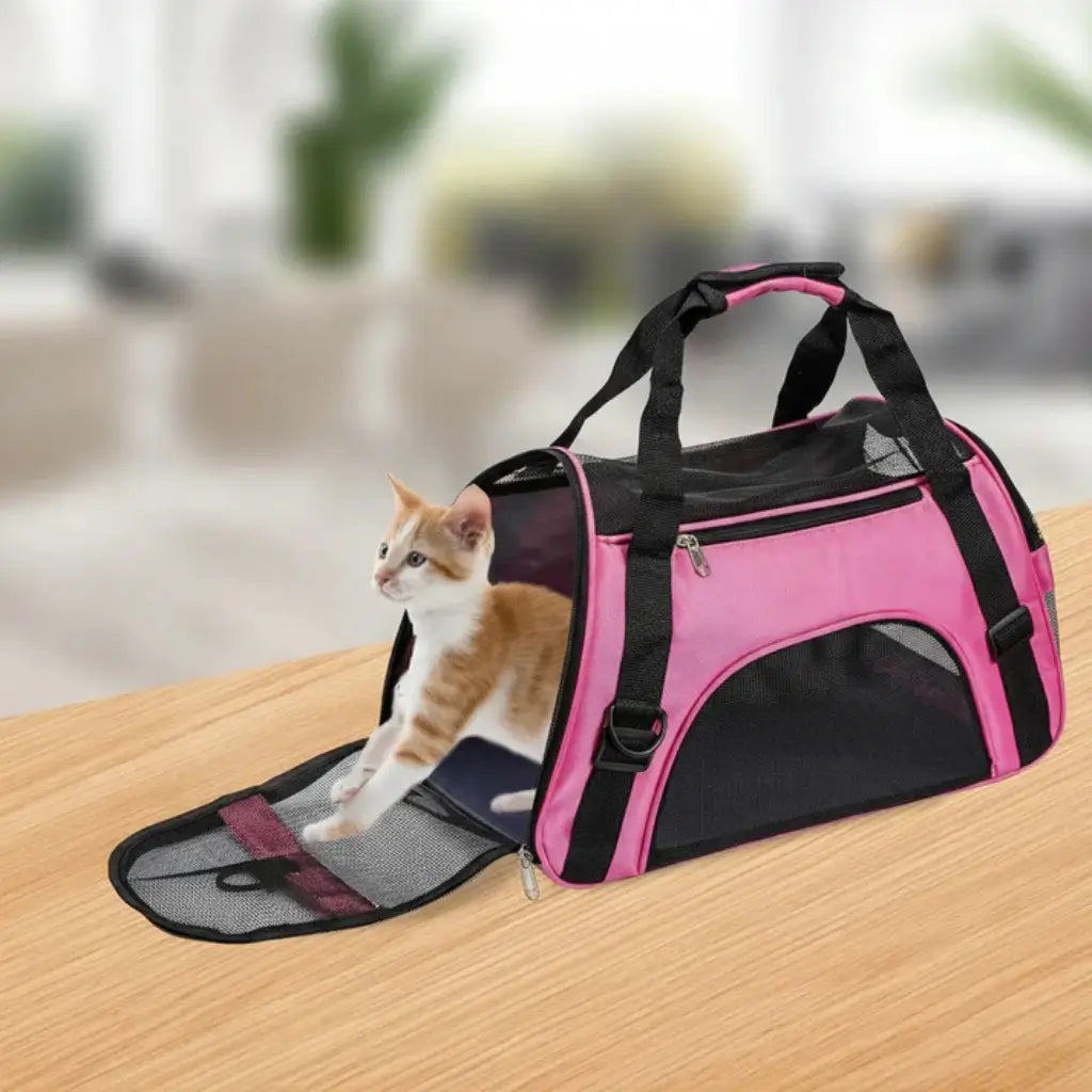 Pink and black pet carrier with a cat inside on a wooden surface