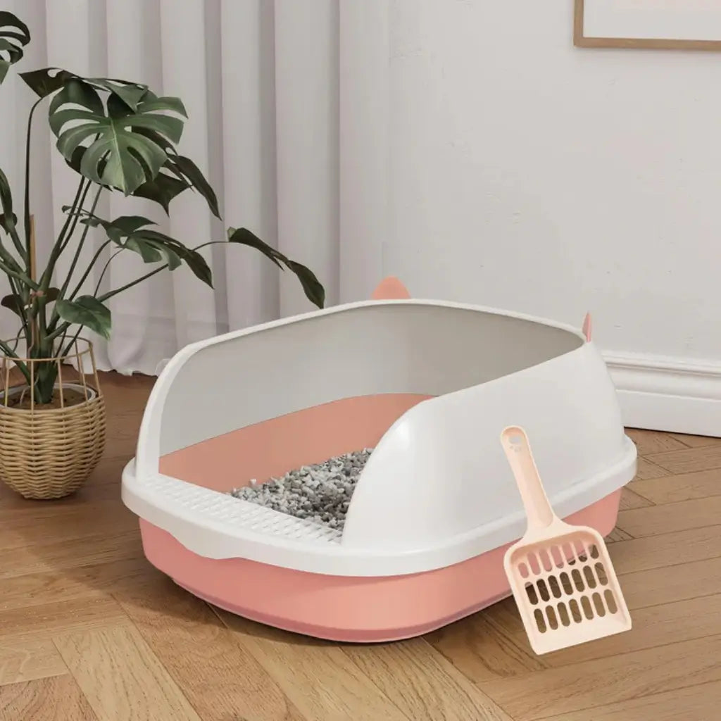 Pink and white pet litter box with a scoop on a wooden floor
