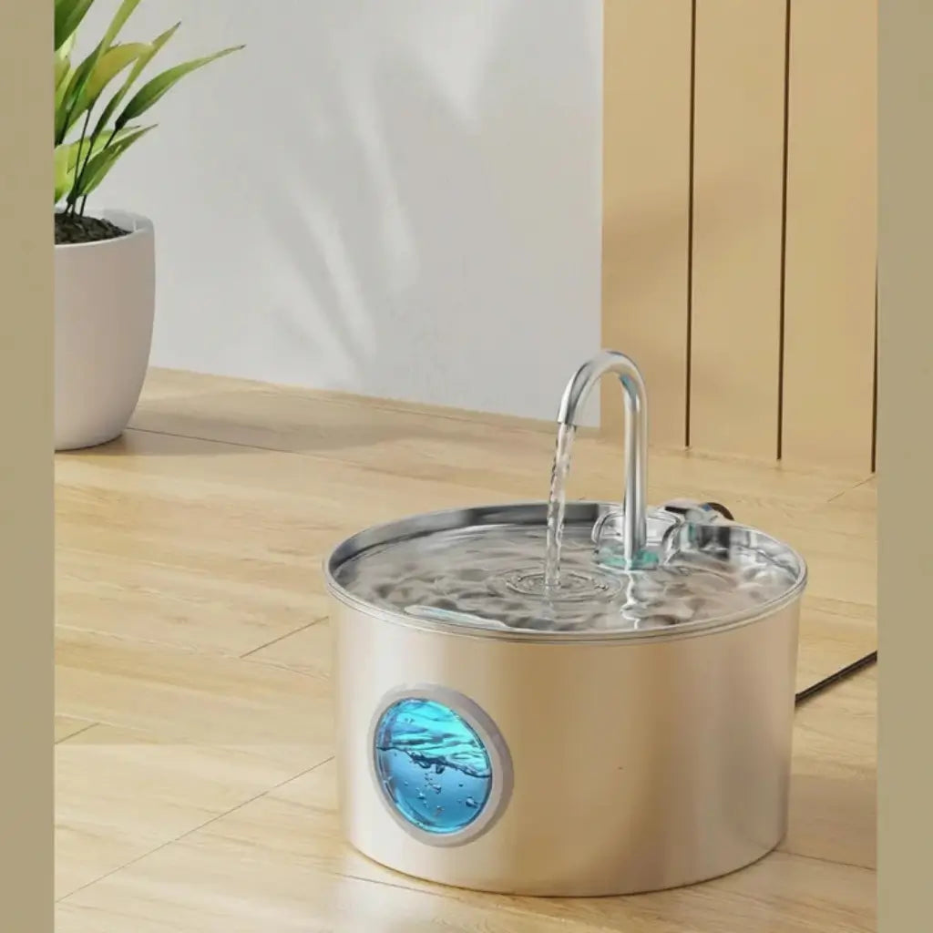 Stainless steel pet water fountain on a wooden floor with a plant in the background