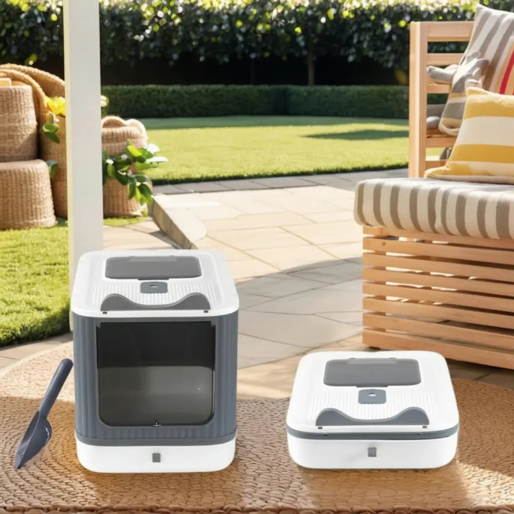 Two cat litter boxes on a patio with outdoor furniture and greenery in the background