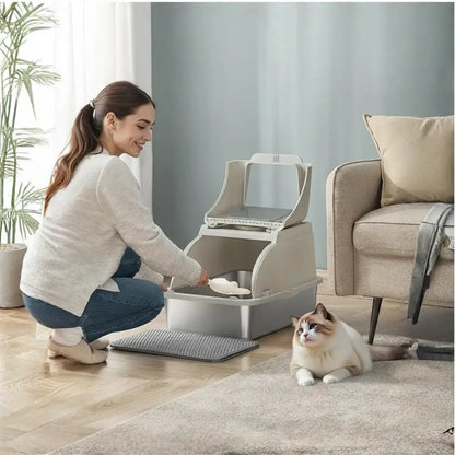 Woman cleaning a cat litter box with a cat sitting nearby in a living room